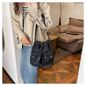 Detail view of a black drawstring bucket bag with two utility front pockets and metal buckles