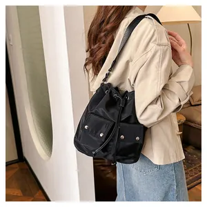 Detail of a black nylon drawstring bucket bag with double front flap pockets and wide strap