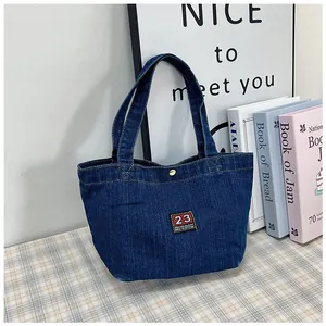 Detail of dark blue denim tote bag with vintage embroidery and gold metal snap button