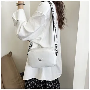Détail du sac à bandoulière en nylon blanc avec papillon et sangle large imprimée