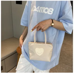 Close-up of beige nylon mini tote bag with a heart smiley face patch held by a model