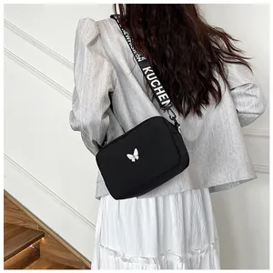 Gros plan d'un sac bandoulière en nylon noir avec motif papillon et large sangle