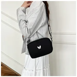 Détail du sac bandoulière en nylon noir avec patch papillon et large sangle lettrée