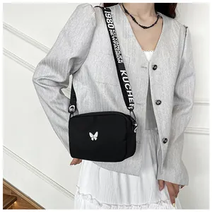 Détail d'un sac bandoulière en nylon noir avec papillon blanc et large sangle stylée