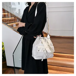 White nylon drawstring bucket bag with side pocket shown on shoulder in modern interior