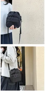 Detail of black nylon drawstring bucket bag showing front zipper pocket and adjustable strap