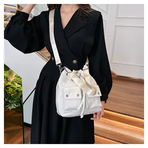 White nylon bucket bag with drawstring closure and two front pockets shown on shoulder