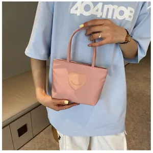Close-up of a pink nylon mini tote bag with a heart smiley face patch and thin handles