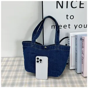 Detail of small dark blue denim tote bag with gold snap button and phone for size reference