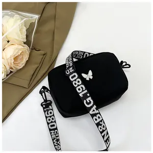 Détail du sac carré en nylon avec logo papillon et bandoulière lettrée jacquard