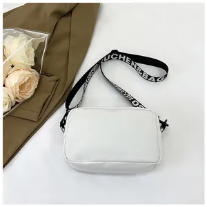 Détail du sac carré en nylon blanc avec large bandoulière réglable imprimée de lettres