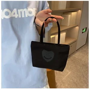 Detail of black mini nylon tote bag featuring a leather heart smiley patch and soft handles