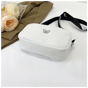 Détail du sac bandoulière en nylon blanc avec logo papillon et large sangle lettrée