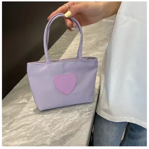 Detail of a purple nylon tote bag featuring a stitched heart patch and double handles