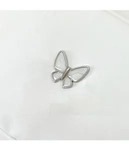 Détail macro du fermoir papillon en métal argenté et émail blanc sur le sac