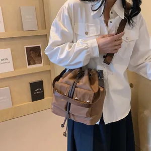 Brown nylon drawstring bucket bag with dual front pockets and wide shoulder strap for women