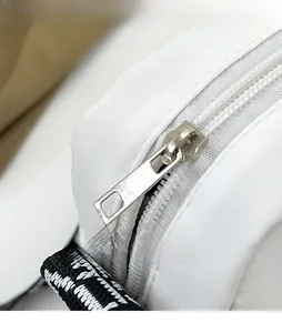 Détail macro du curseur de fermeture en métal argenté sur un sac bandoulière blanc en nylon