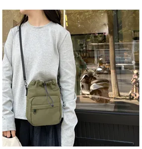 Detailed view of olive green nylon bucket bag featuring a black drawstring and front zipper