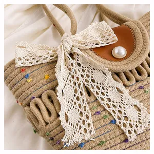 Détail du sac cabas tissé avec nœud en dentelle blanche, boucle perle et pompons colorés