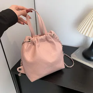 Pink quilted leather drawstring bucket bag with chain strap shown in a home setting
