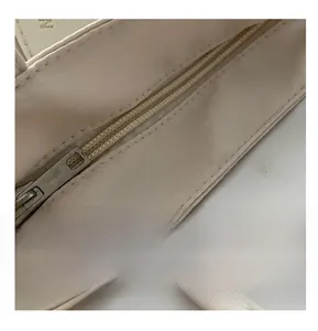 Detailed close-up of smooth zipper closure and metal puller on beige nylon mini bag