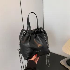 Black quilted bucket bag with silver chain strap and drawstring closure held by hand
