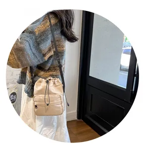 Detail view of beige nylon bucket bag with black zip pocket and adjustable strap
