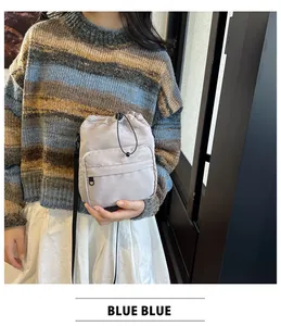 Detail of light grey nylon drawstring bucket bag with zippered front pocket worn by model