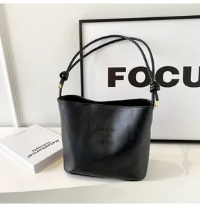 Detail of black suede bucket bag featuring embossed text and gold metal strap tips