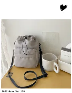 Close-up of light gray nylon drawstring bucket bag with black strap on a wooden table
