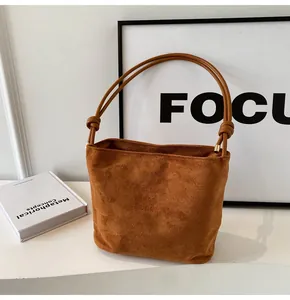 Close-up of brown suede bucket bag featuring knotted handle and fashion embroidery