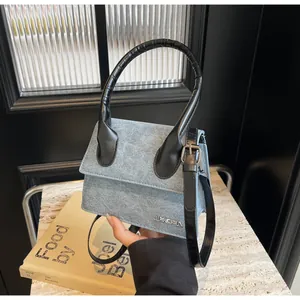 Detalle del mini bolso azul con logotipo metálico JINGPIN y asa negra de cuero