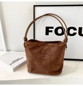Detail of brown suede bucket bag featuring embossed text and knotted strap with gold tips