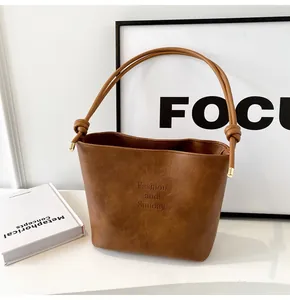 Detail of caramel suede bucket bag featuring knotted shoulder strap and gold hardware accents