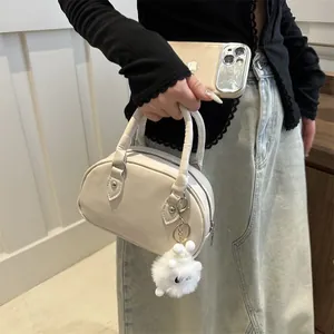 Elegante borsa a mano bowling bianco crema con ciondolo pompon in una scena di stile