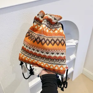 Borsa a secchiello etnica intrecciata con motivi geometrici e nappe tenuta in mano