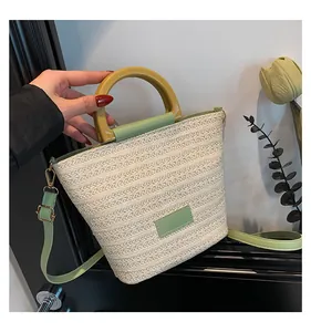 Détail macro du sac seau en paille avec garniture en cuir vert et poignée en bois