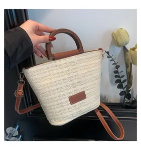 Détail d'un sac seau en paille tressée avec poignée en bois et bandoulière en cuir