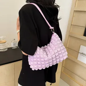 Gros plan d'un sac à bandoulière violet texturé porté par un mannequin dans un décor