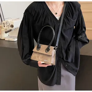 Detalle de un mini bolso bandolera marrón con asa negra y logotipo metálico plateado