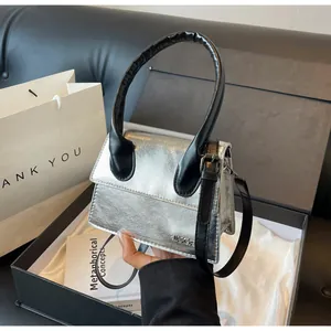 Detalle de mini bolso plateado metalizado con asa negra en caja de regalo de lujo