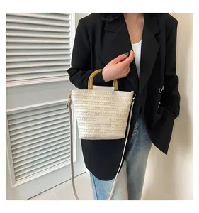 Détail du sac seau en paille tressée beige avec poignée ronde en bois jaune et bandoulière