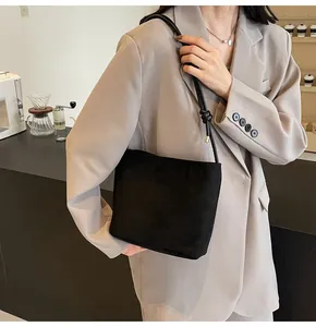 Detail view of black suede bucket bag with adjustable strap on a grey suit jacket