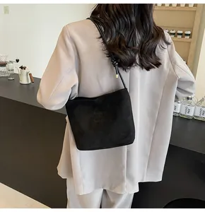 Detail of black suede tote bag with printed text on shoulder of model in a cafe