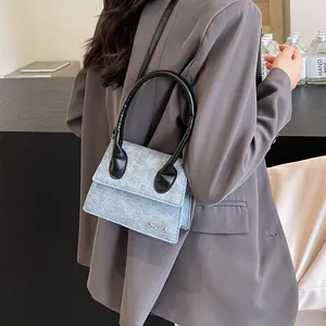 Bolso bandolera de mezclilla azul claro con asa negra y colgante de logo metálico JINGPIN