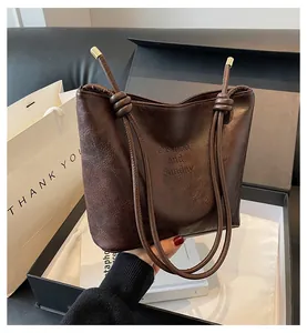 Close-up of brown suede bucket bag featuring elegant knot strap and debossed logo detail