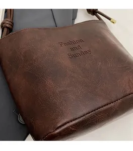 Detail of brown suede bucket bag featuring Fashion and Sunday embossed text and knot strap