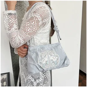 Ricamo dettagliato di motivi floreali e nuvole bianche su una borsa blu-grigio chiaro
