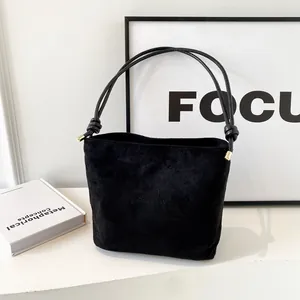 Minimalist black suede bucket bag with double cord handles and gold metal details