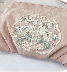 Ricamo dettagliato con motivi floreali tradizionali su trama plissettata rosa della borsa